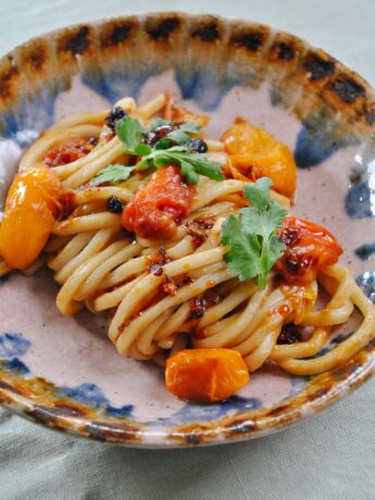 Bowl of noodles covered in soft cooked tomatoes and chilli oil.