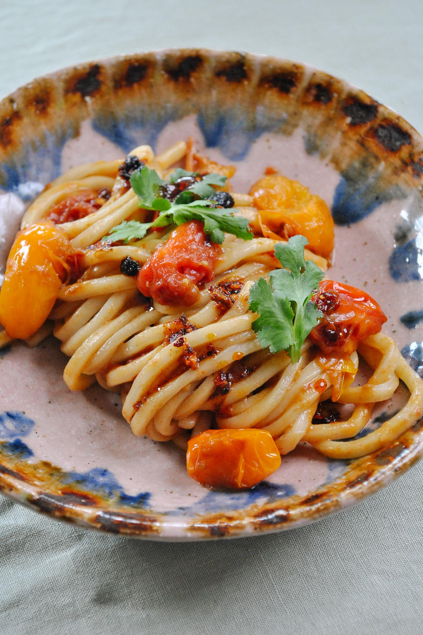 Bowl of noodles covered in soft cooked tomatoes and chilli oil.